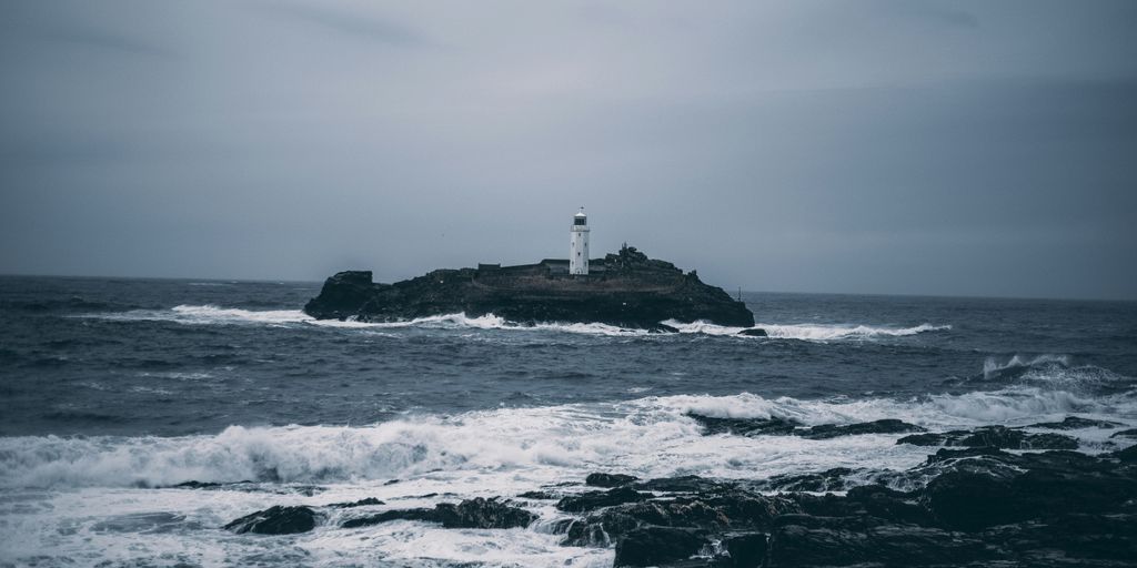 white lighthouse on rock formation surrounded by ocean